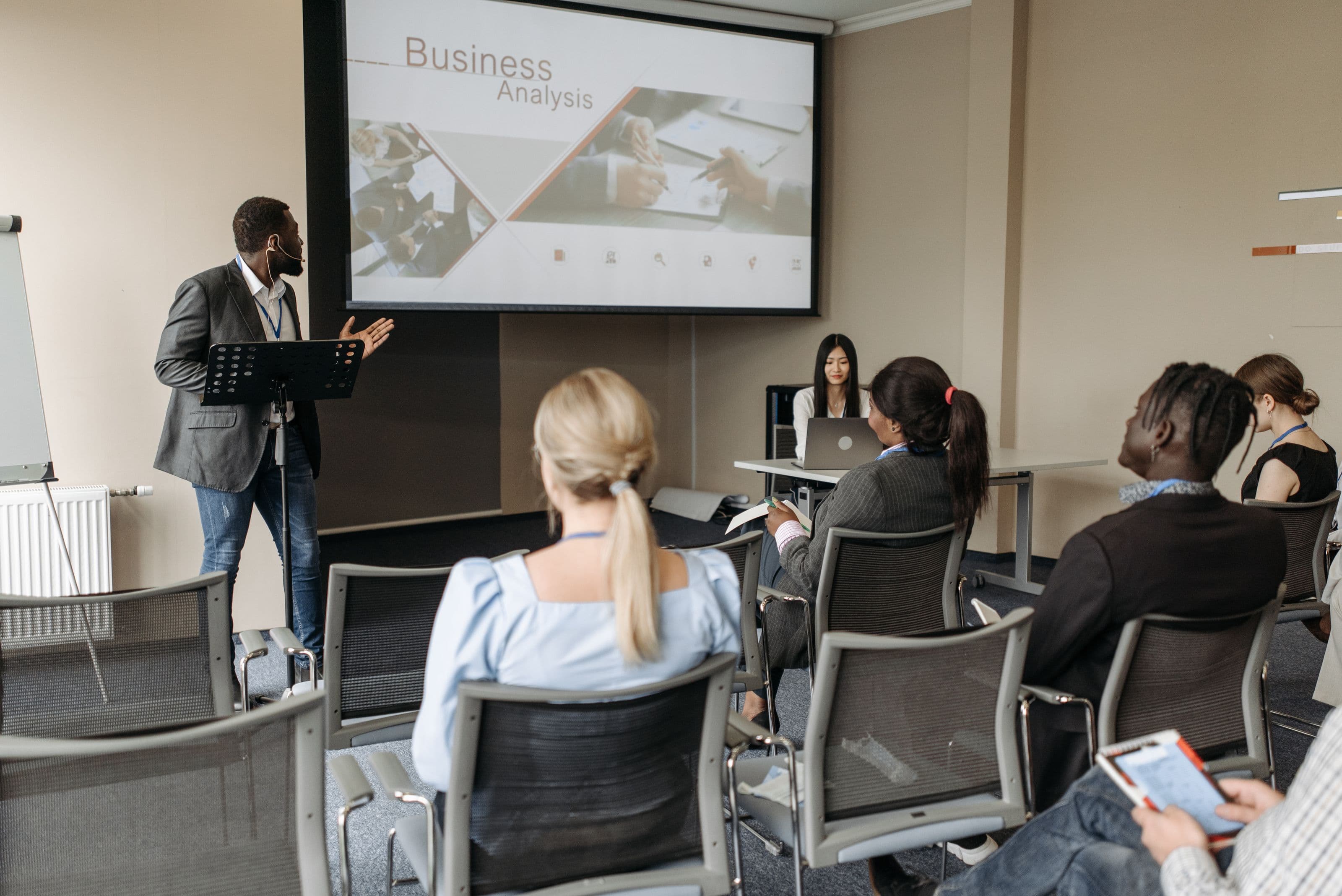 Een diverse groep deelnemers luistert aandachtig naar een spreker tijdens een training in een lichte zaal, een warm beeld bij een workshop met een verzorgde pauze