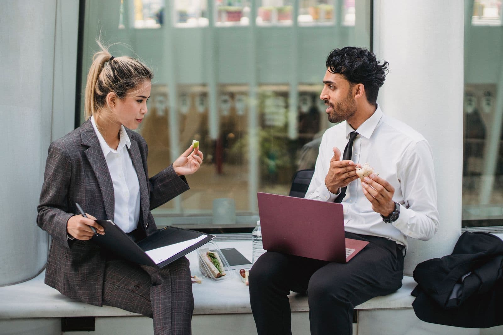 Twee collega's in pak overleggen tijdens een zakelijke lunch met een laptop en een verzorgde lunch op tafel