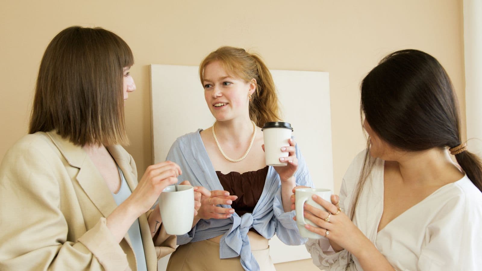 Drie collega's staan te praten met een kop koffie in de hand tijdens een informele pauze op kantoor