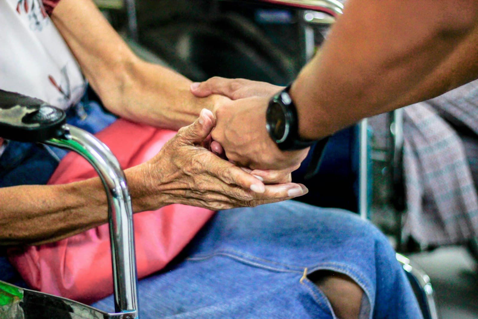 Een jongere hand houdt liefdevol de hand van een oudere persoon vast, een beeld van aandacht en toewijding in de zorg