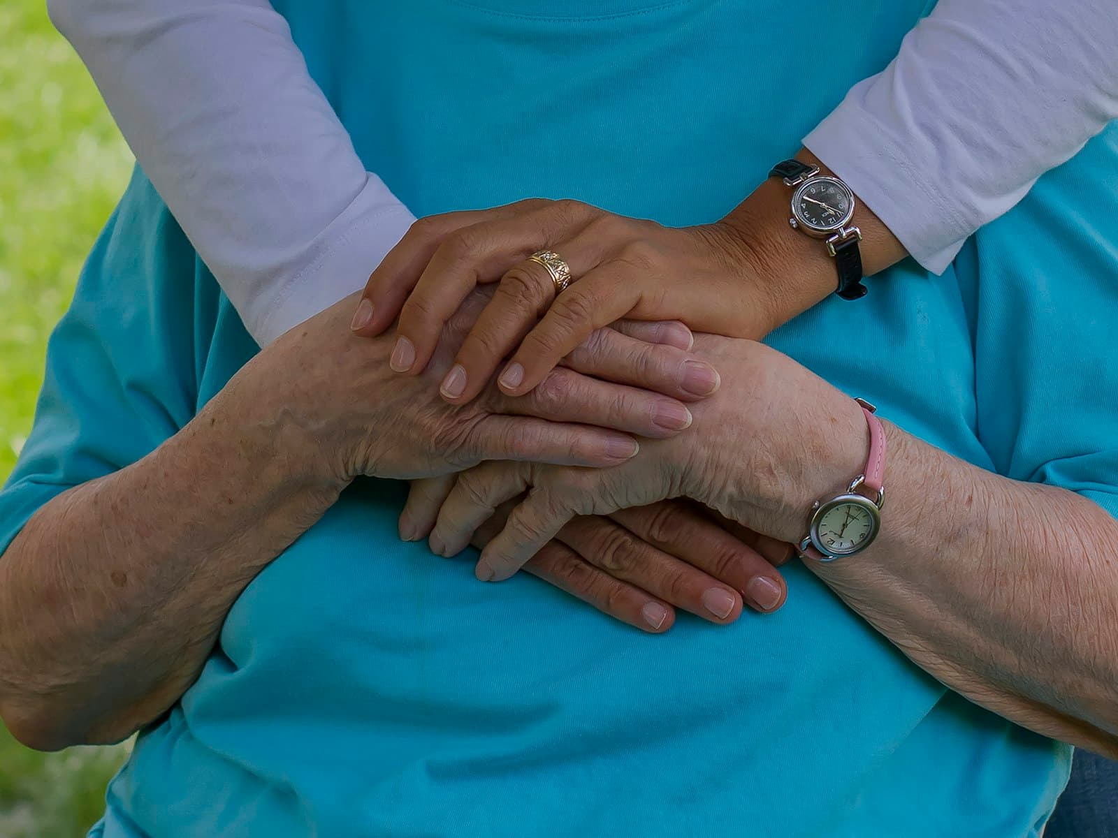 Twee armen omhelzen liefdevol een oudere persoon in een lichtblauwe trui, een warm beeld bij koekjes bestellen voor de zorg